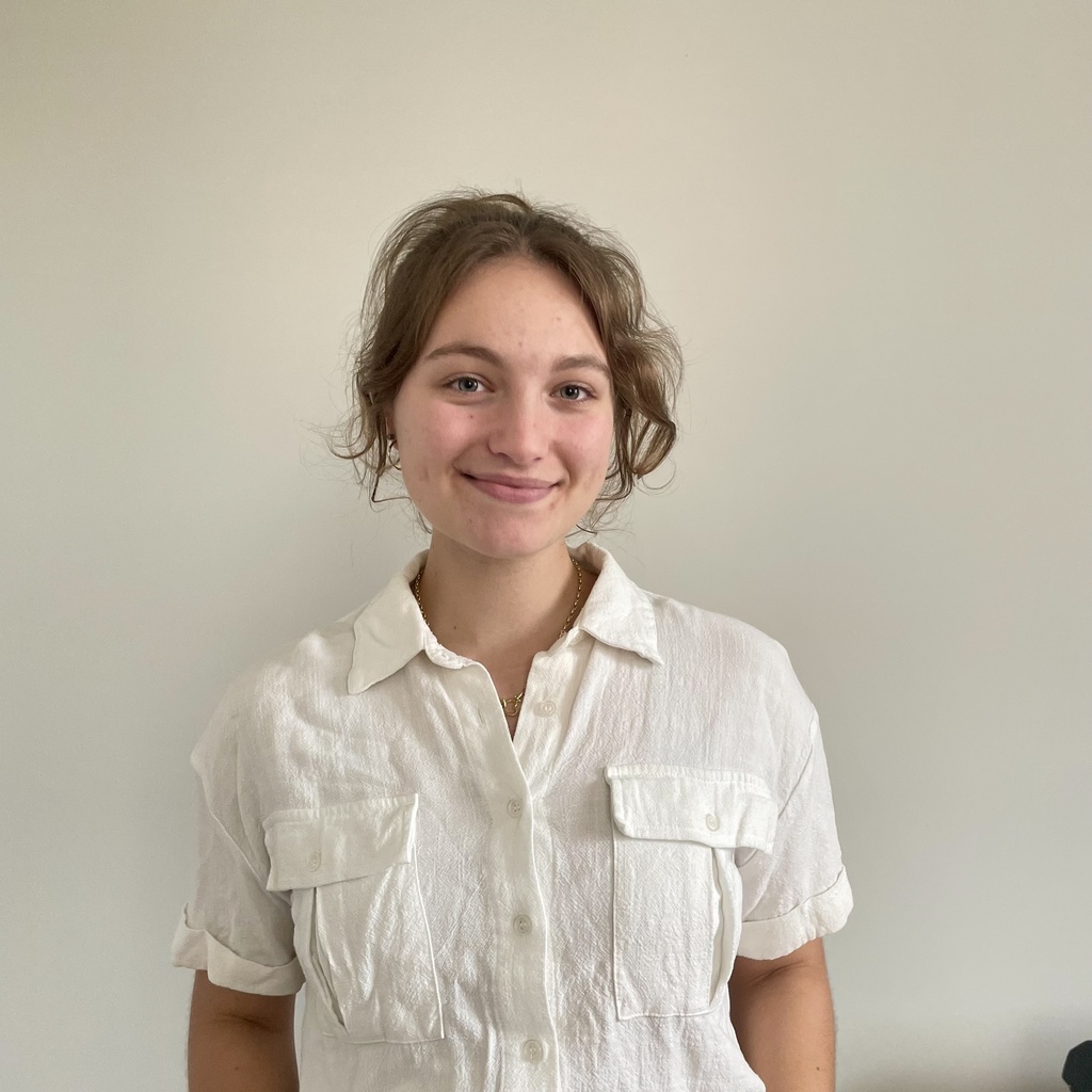 A photo of Ciara Tapanes standing in front of a white wall wearing a white shirt. 